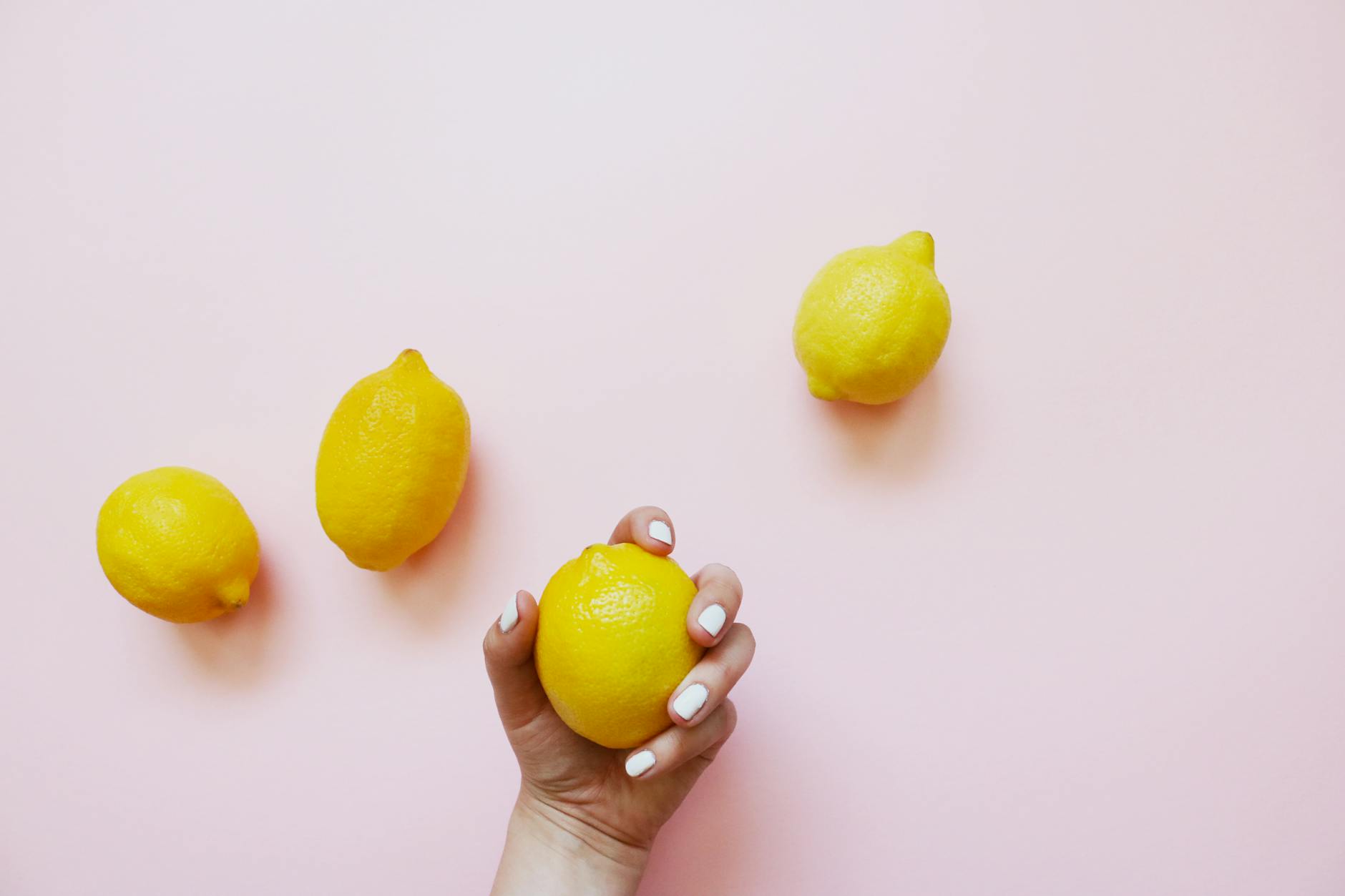 A hand holding a lemon on a soft pink background, symbolizing the transition and renewal of perimenopause pleasure