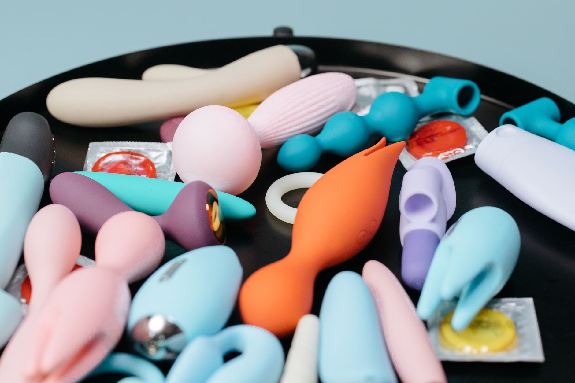 A vibrant collection of various clitoral vibrators on a black tray, featuring diverse shapes and colors.