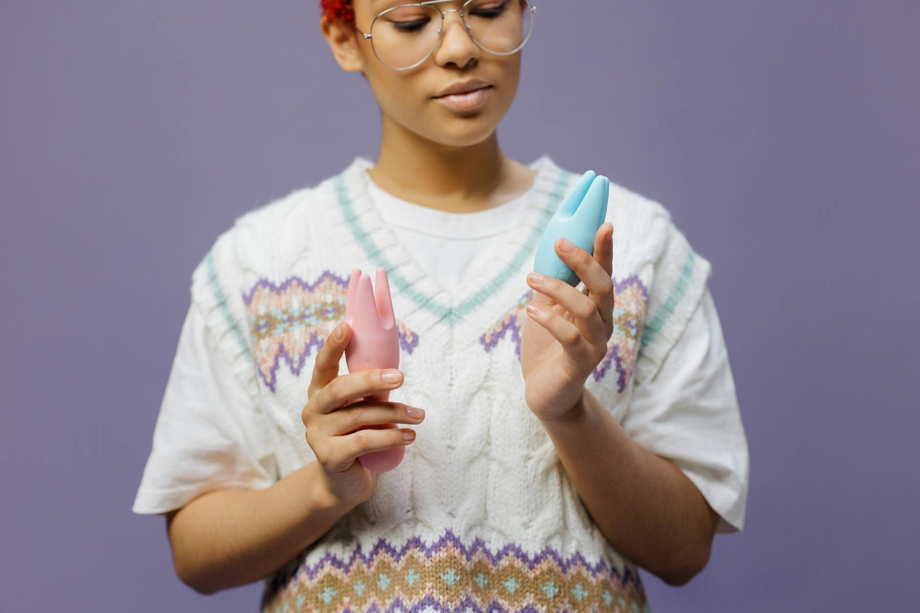 Woman thoughtfully holding blue and pink vibrators, representing postpartum pleasure recovery